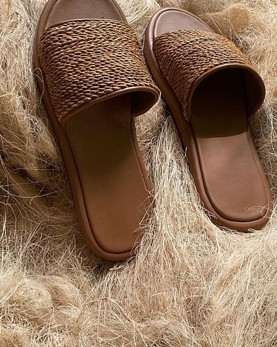 A pair of woven plantain fibre slippers resting on raw fibre